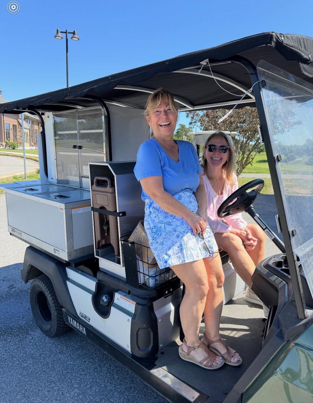 Lisa Grenis and Jana Post sharing a laugh on a golf cart at a Calvert County community event