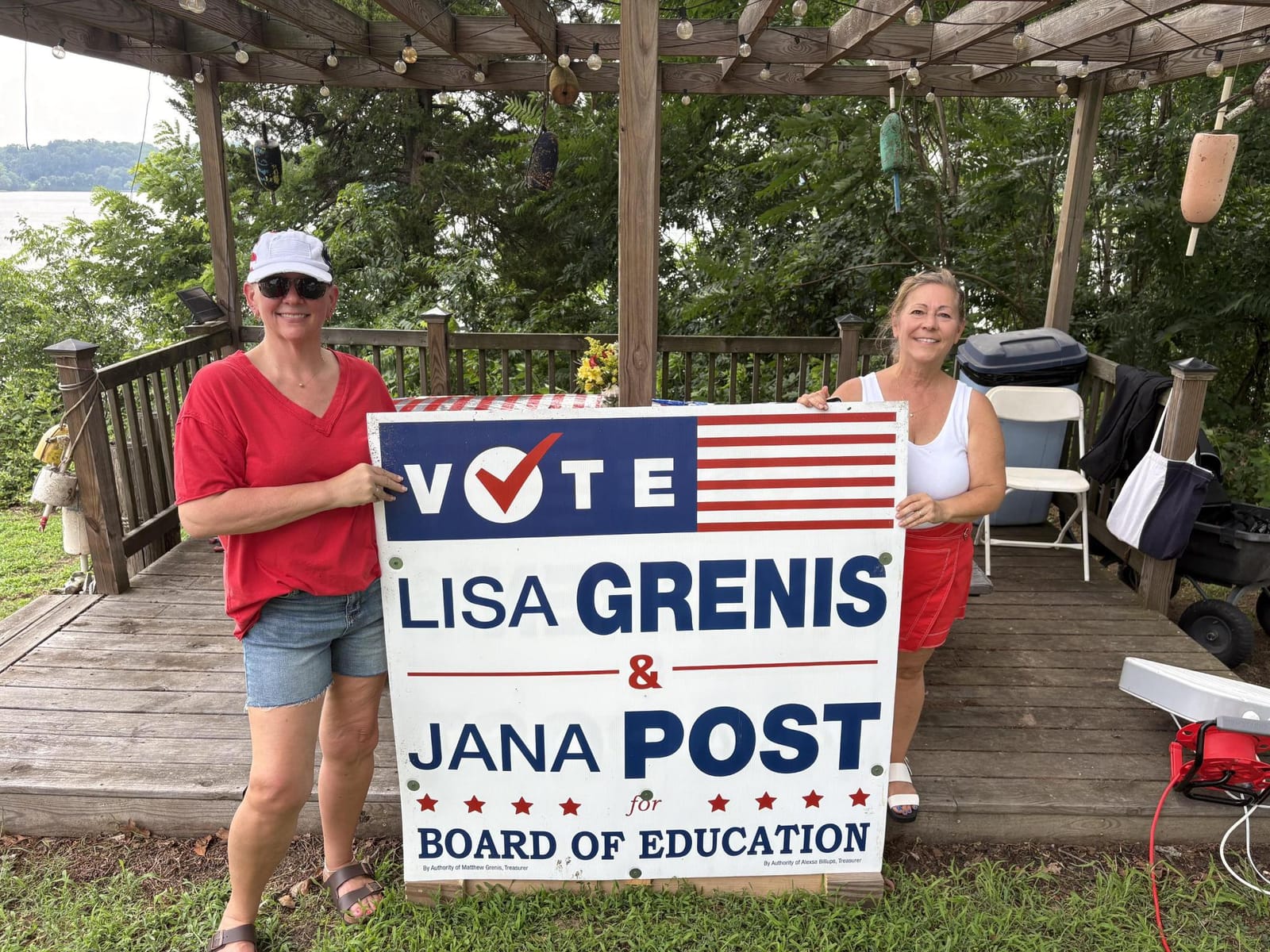 Lisa Grenis and Jana Post holding their campaign sign at a waterfront pavilion in Calvert County